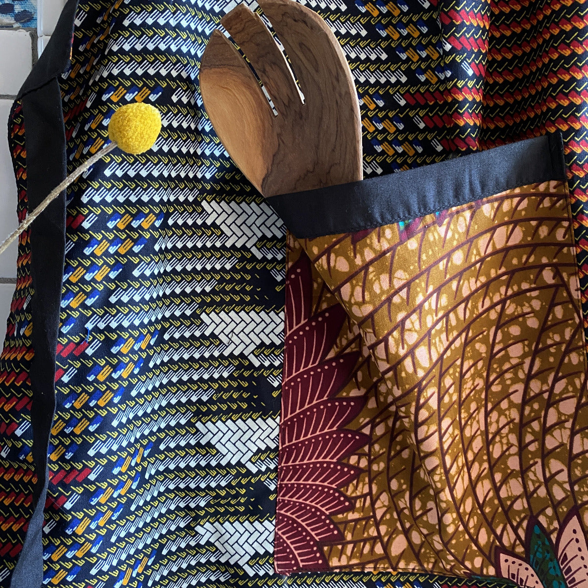 Detail of Handcrafted African wax print apron made in Uganda. Perfect for housewarming and wedding gitfs. Excellent for entertaining guests during the holidays, Thankgiving, Christmas, and more. Shown with olivewood salad server.