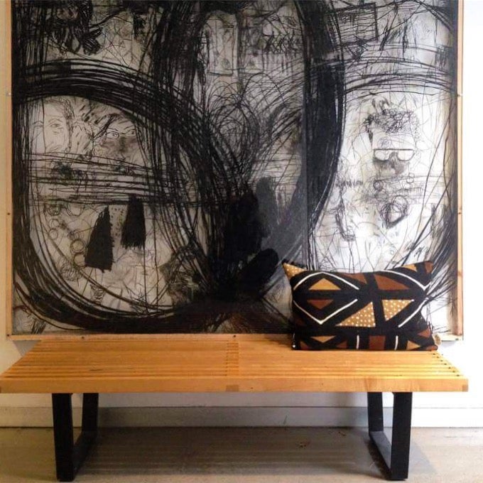 Brown, black, and white mudcloth pillows with geometric designs styled on Scandinavian bench. Modern pillows made in USA, designed in Mali. Seen here with African art.